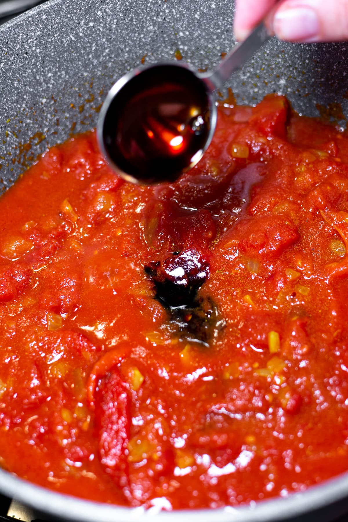 Pouring Pomegranate Sauce over a pan with tomato sauce.