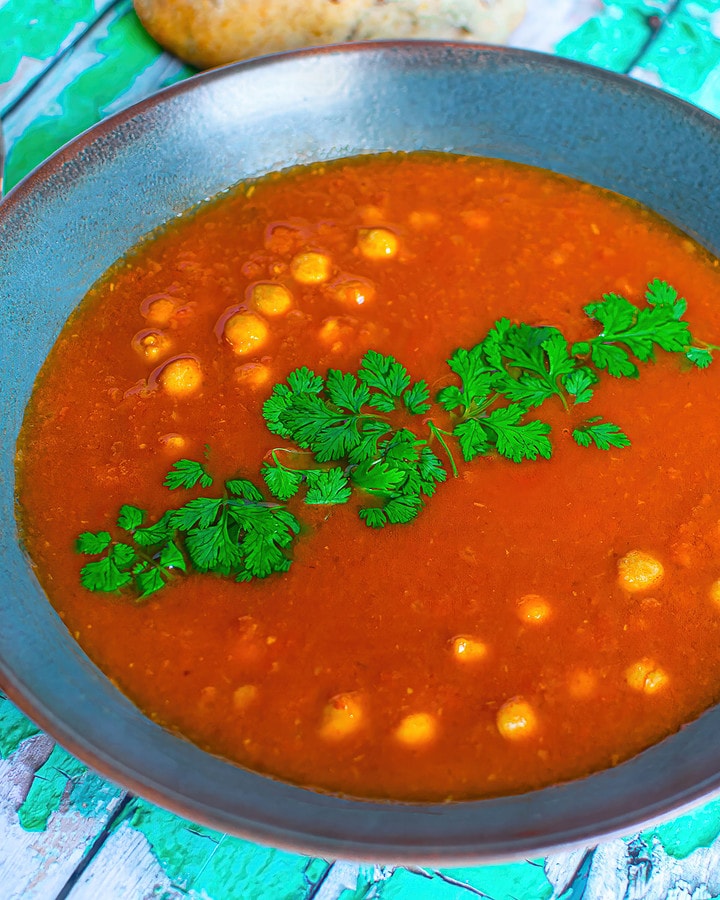 Close up view of chickpea soup with tomatoes and bell peppers.