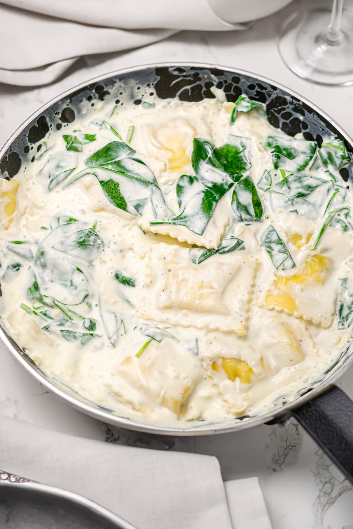 Creamy spinach and cheese ravioli in a iron skillet on a white marble surface.