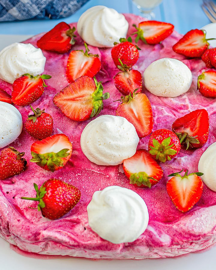 Strawberry pavlova with fresh strawberries on a white serving cake plate.