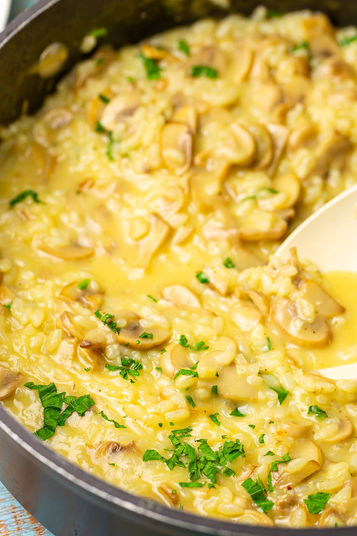 Creamy mushroom risotto in a pan with a white spoon in it.
