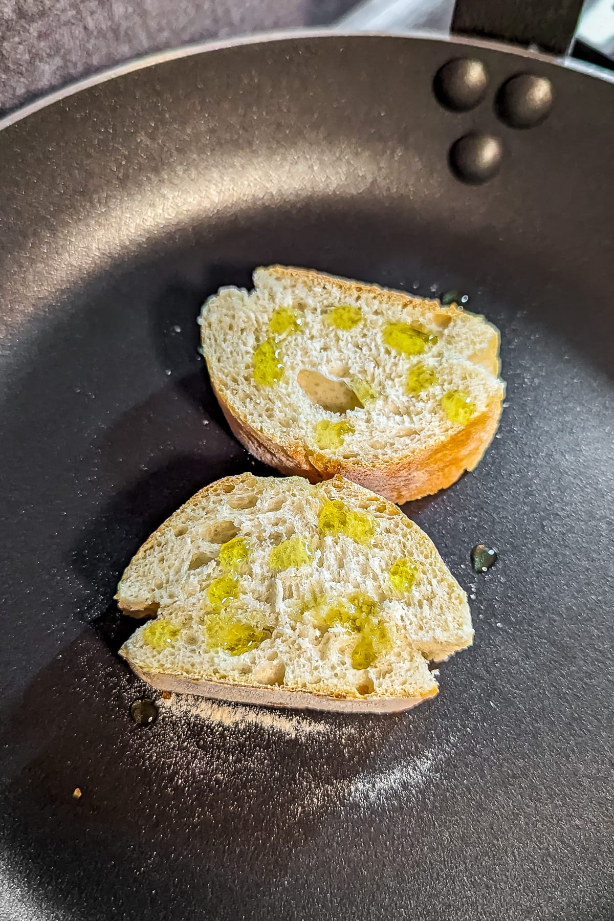 Toasting 2 bread slices on a frying pan with a few splashes of olive oil.