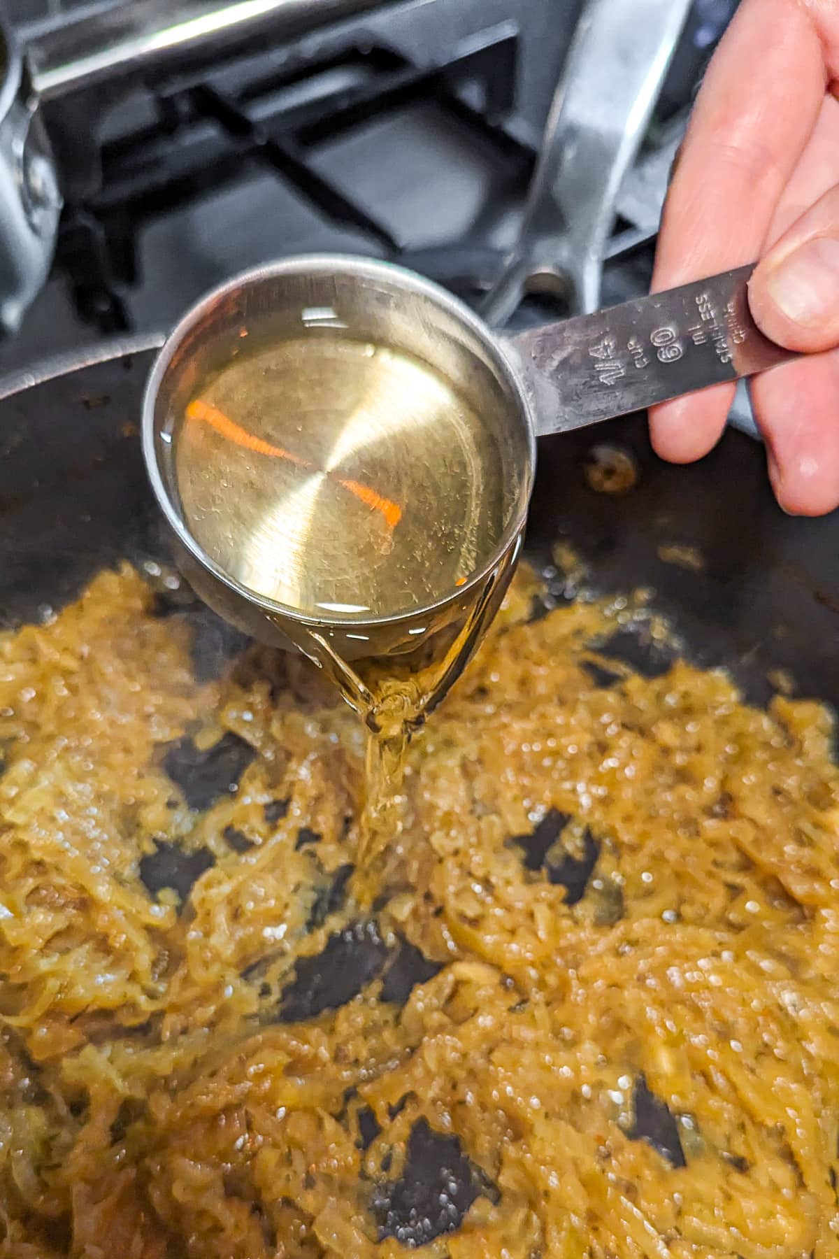 Pouring white wine over caramelized onion in a frying pan.