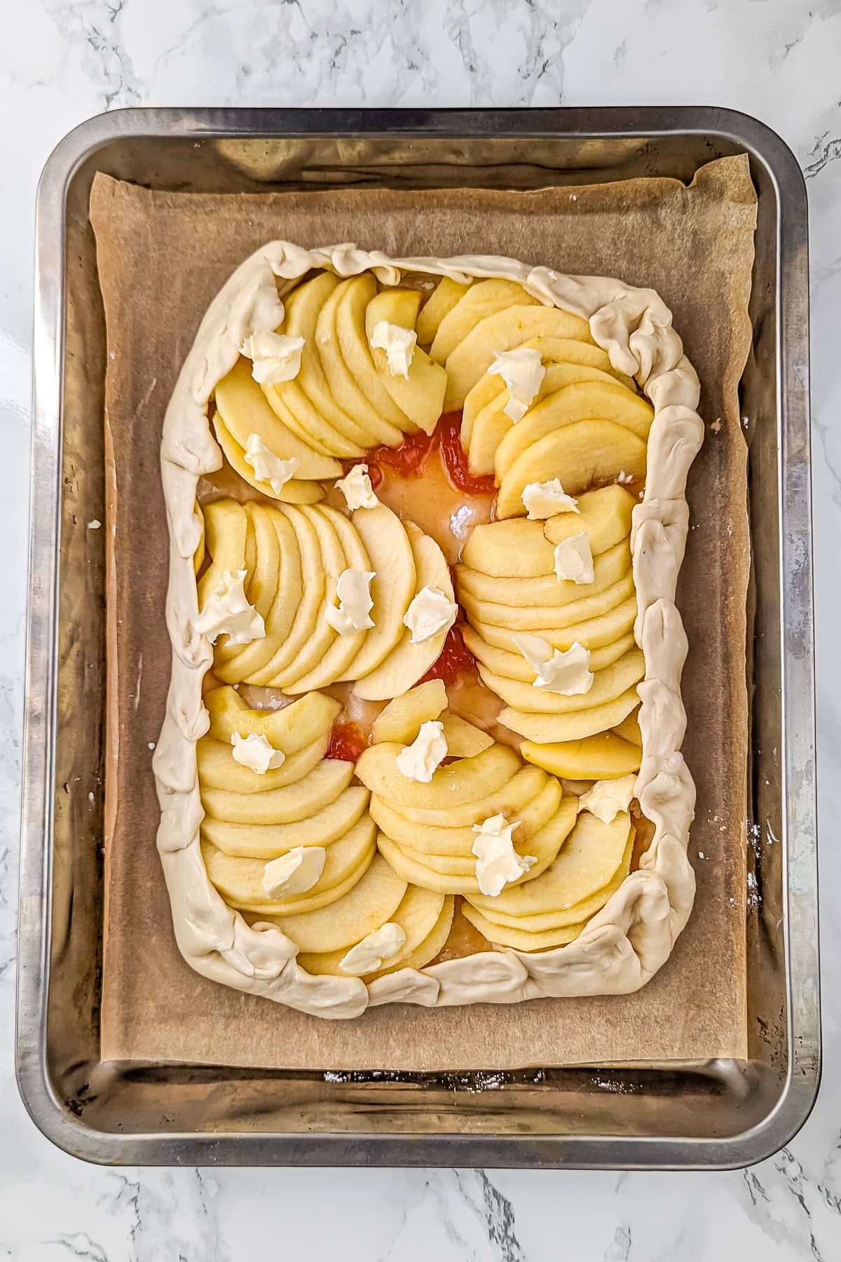 Apple tart assembly completed with layers of apple slices and dots of butter on top, ready to bake.