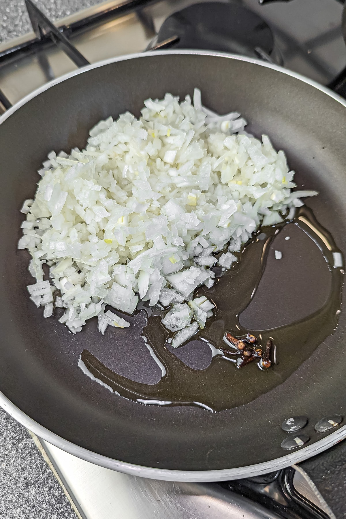 Diced onions and whole cloves of garlic sautéing in oil in a non-stick frying pan, the first step in preparing a savory dish.