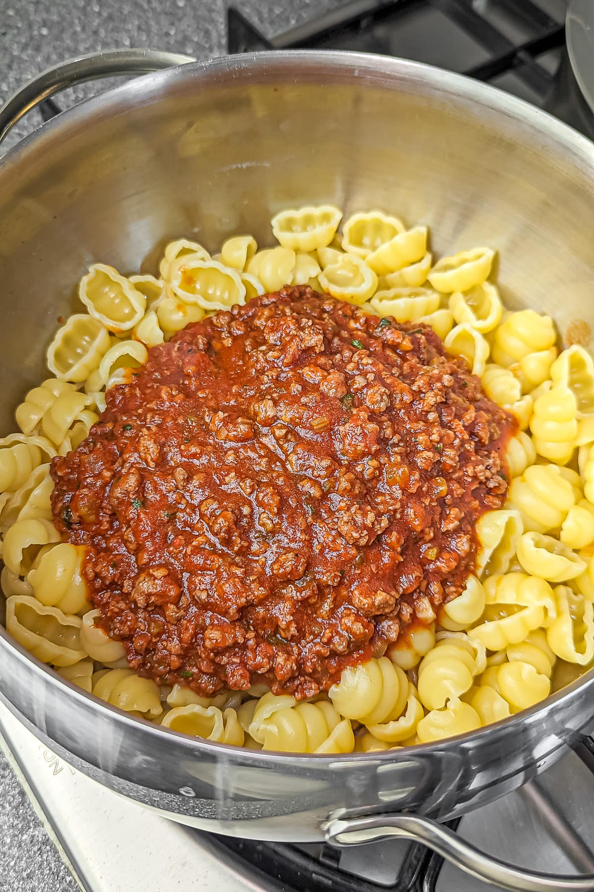 Pasta shells being mixed with bolognese sauce in a large pot.