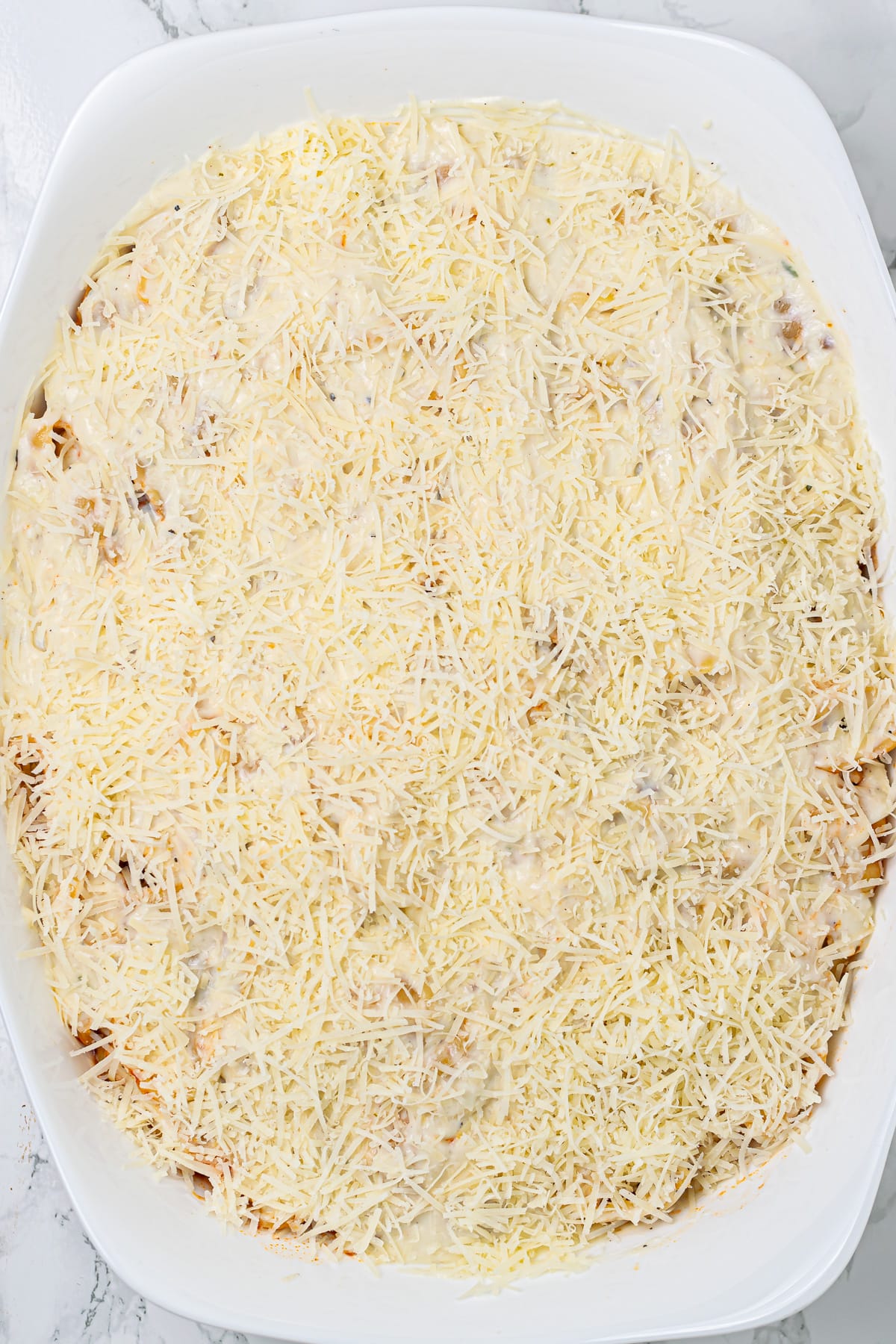 Baked pasta bolognese covered with shredded cheese, before baking.