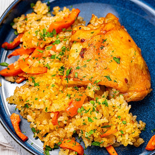 A serving of baked chicken over spiced rice on a blue plate, garnished with herbs.