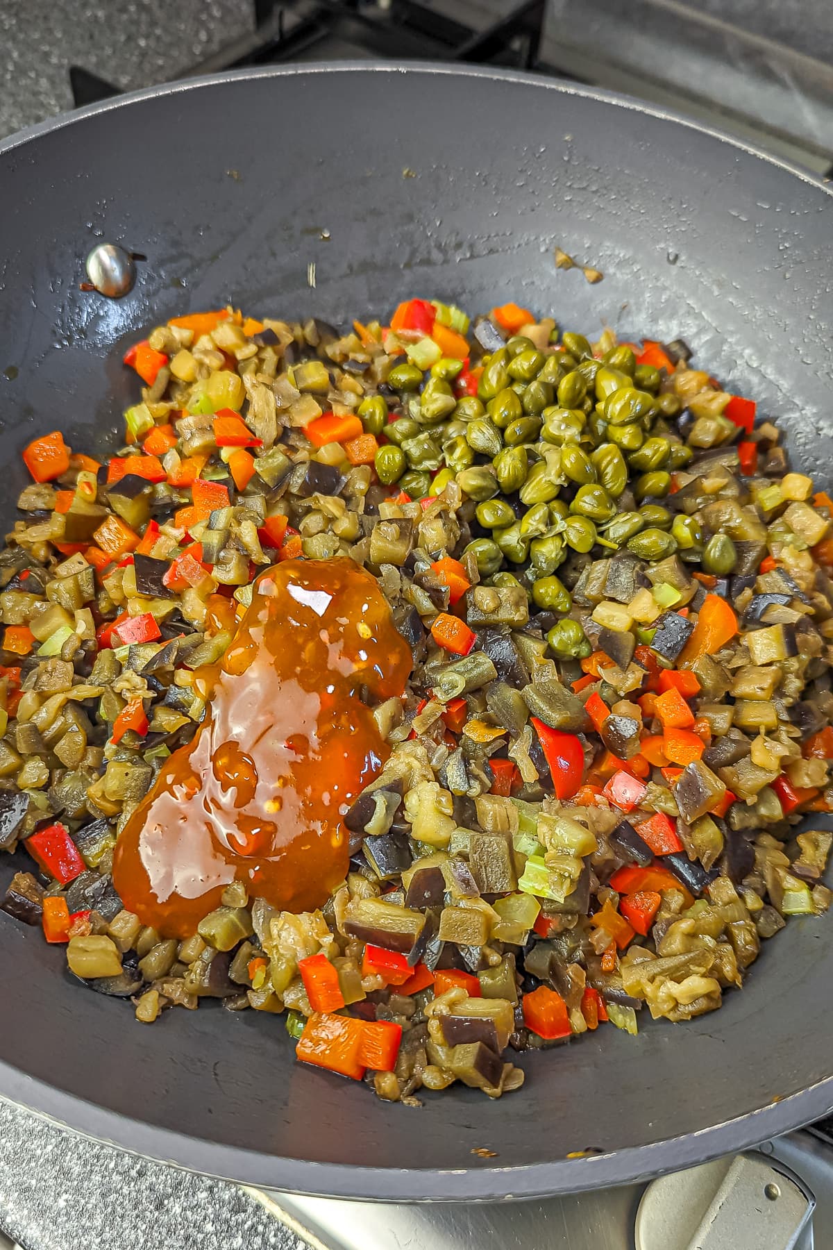 Capers and red sauce introduced to the pan of sautéed vegetables.