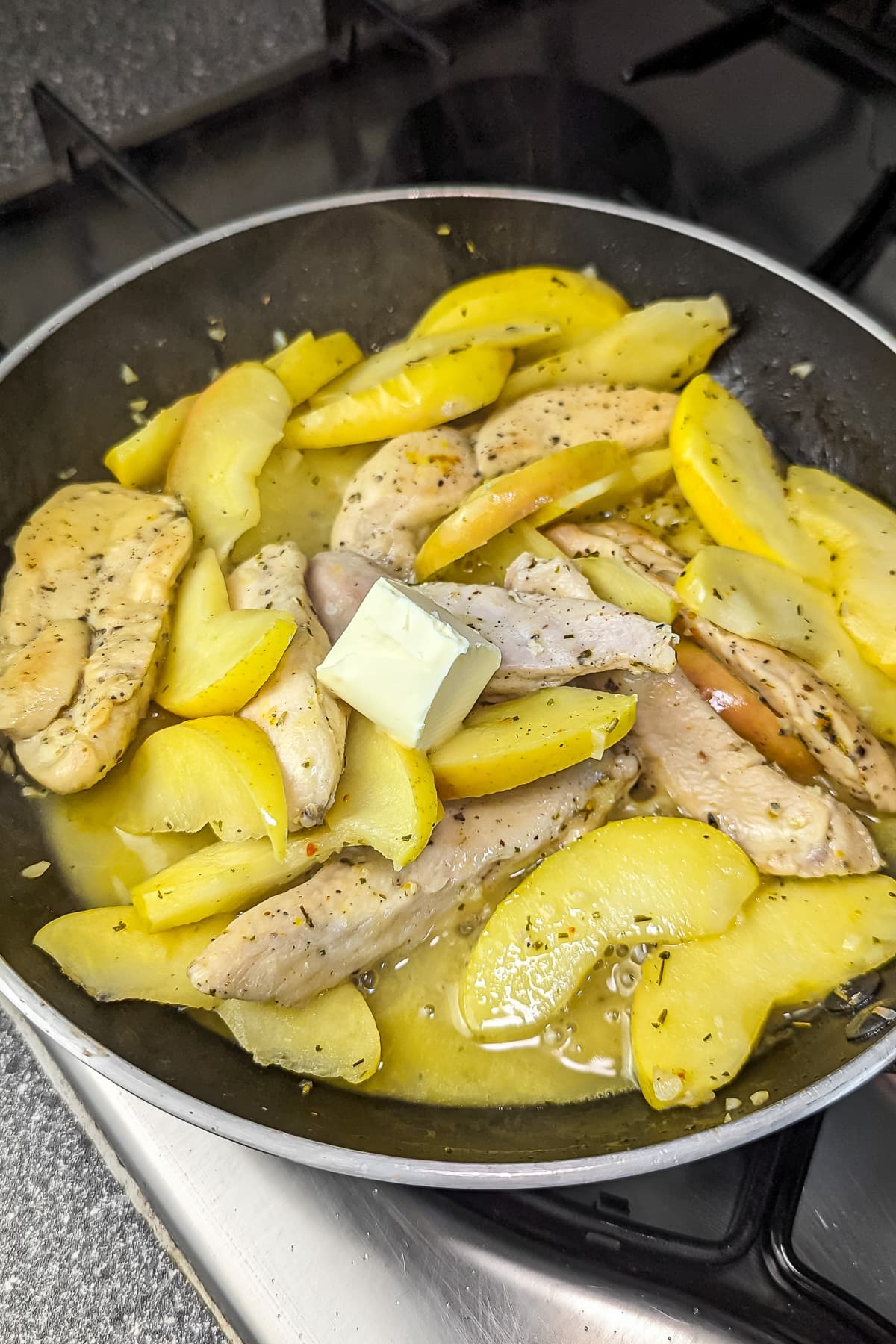 A pat of butter melting over the cooking chicken and apple slices in the skillet.