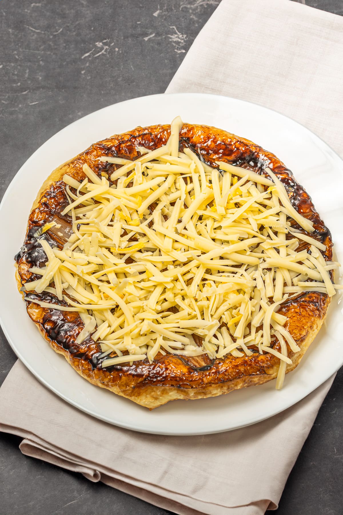 Caramelized onion tart topped with shredded cheese on a white plate.
