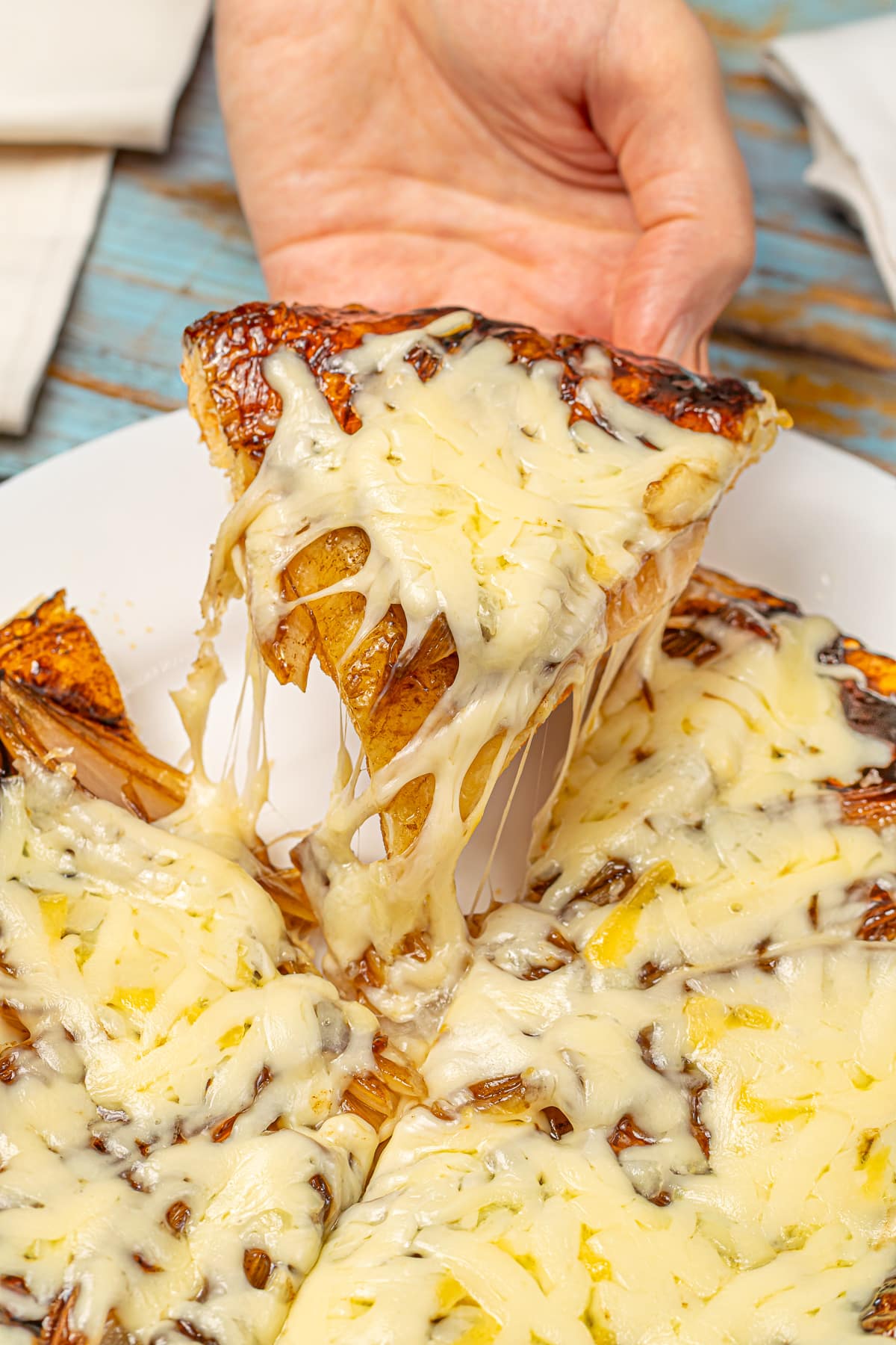 Hand pulling a cheesy slice from a caramelized onion tart, showcasing the melted cheese.