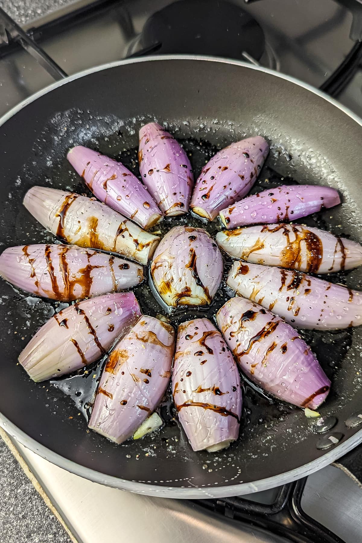 Sliced shallots in a skillet with balsamic glaze, arranged in a circular pattern.