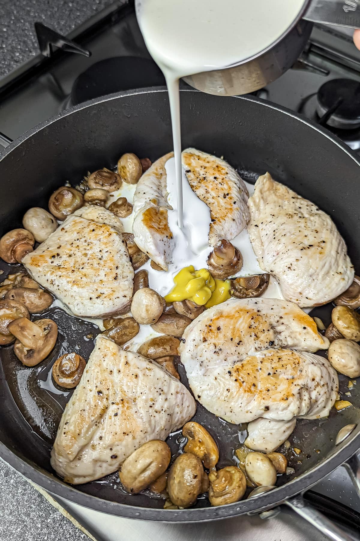 Pouring whipping cream into the sauté pan with seared chicken and golden mushrooms for a rich sauce.