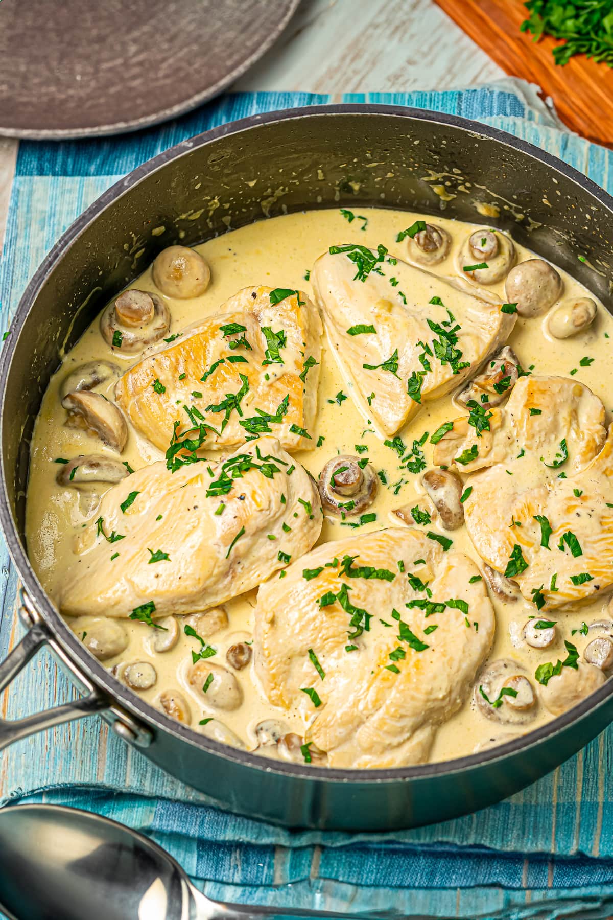 Creamy mushroom sauce simmering with seared chicken breasts in a skillet, garnished with chopped parsley.