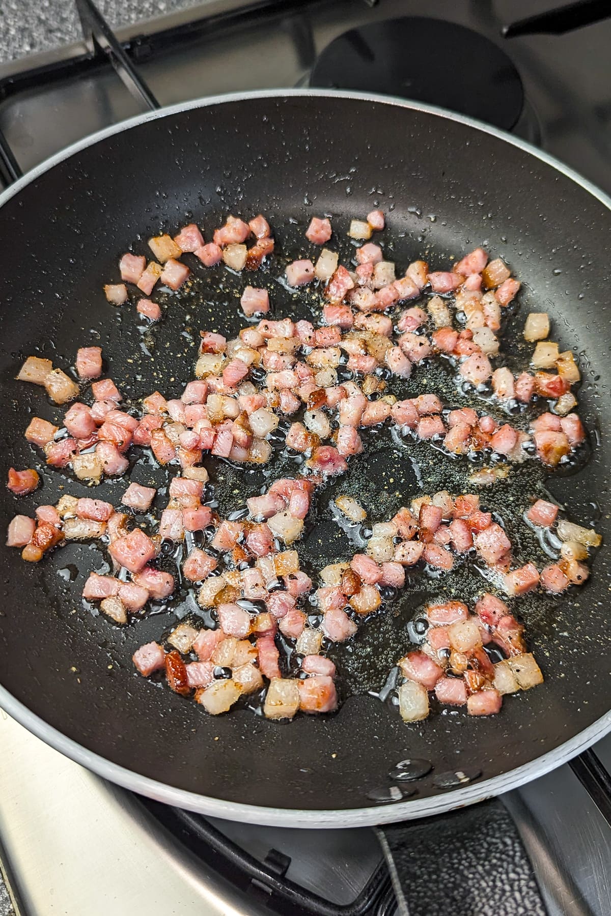 Diced ham sizzling in a black frying pan over a stove.