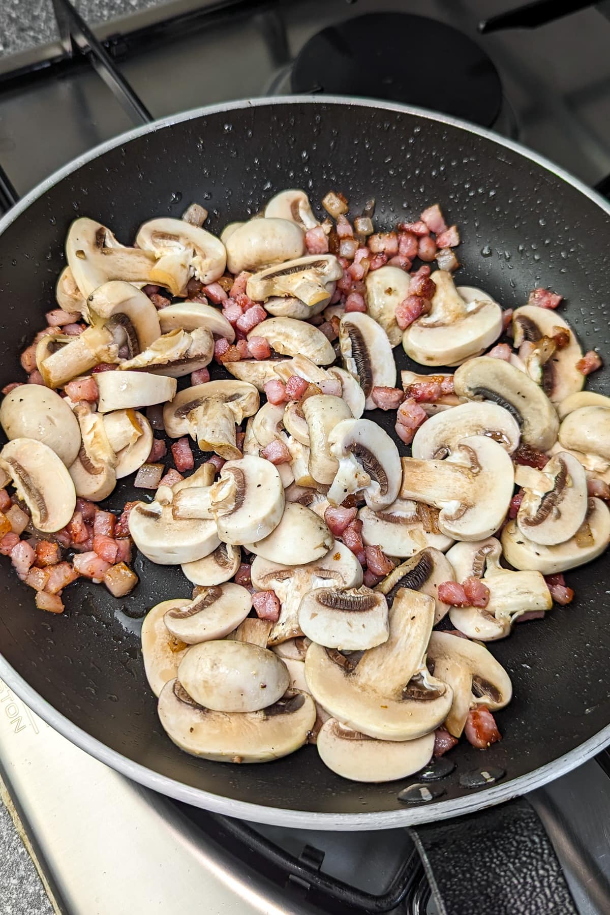 Sliced mushrooms and diced ham being sautéed together in a black frying pan.