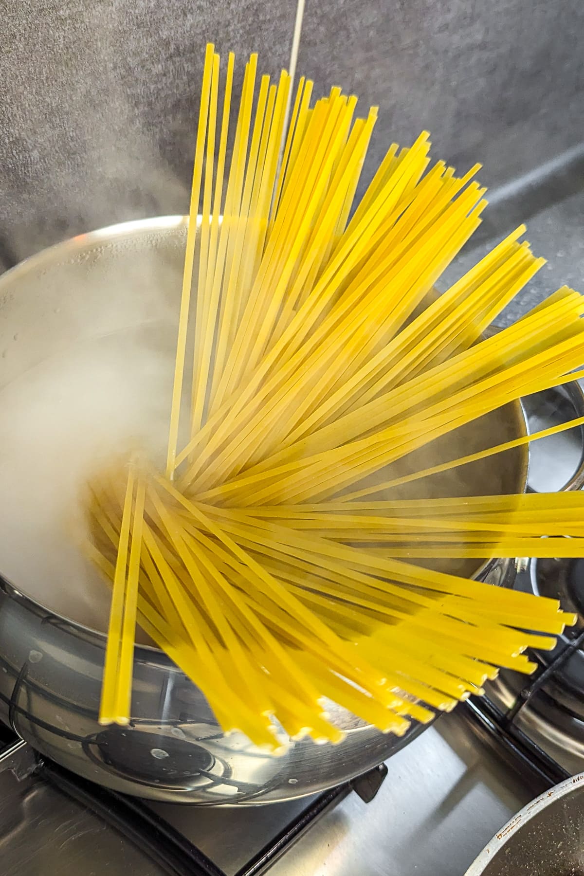 Uncooked spaghetti submerged in boiling water in a stainless steel pot on a stovetop.