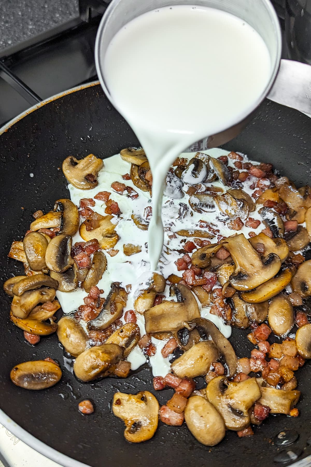 Cream being poured over the sautéed mushrooms and ham in the frying pan.