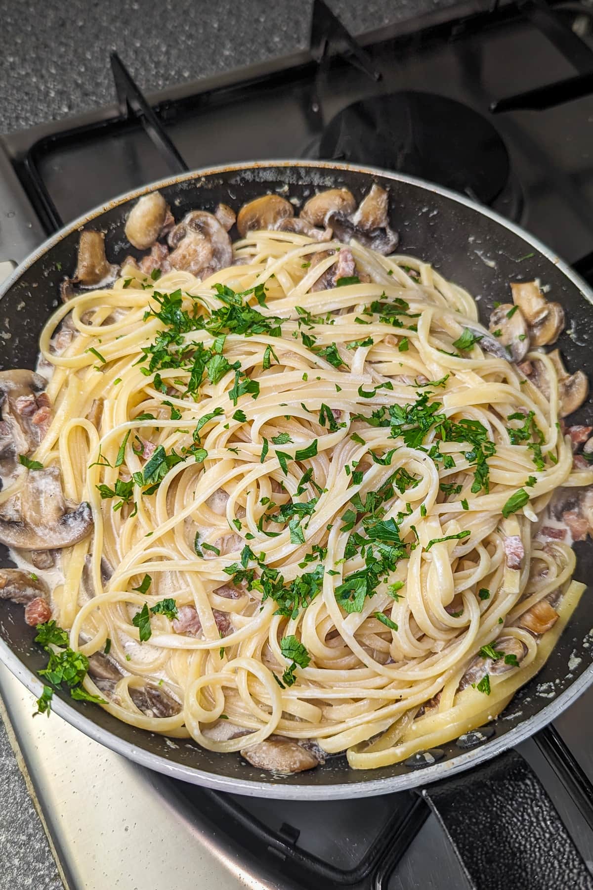 Spaghetti with creamy mushroom and ham sauce in a frying pan, sprinkled with chopped parsley.
