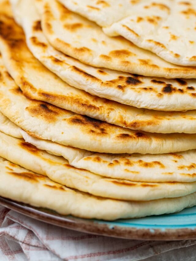 Stack of cooked flatbreads on a teal plate with charred spots visible, suggesting they are freshly grilled.