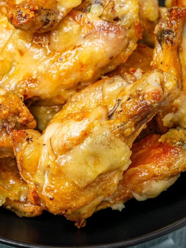 Zoomed-in view of juicy garlic chicken wings served in a black bowl, highlighting the glistening sauce and crispy edges.