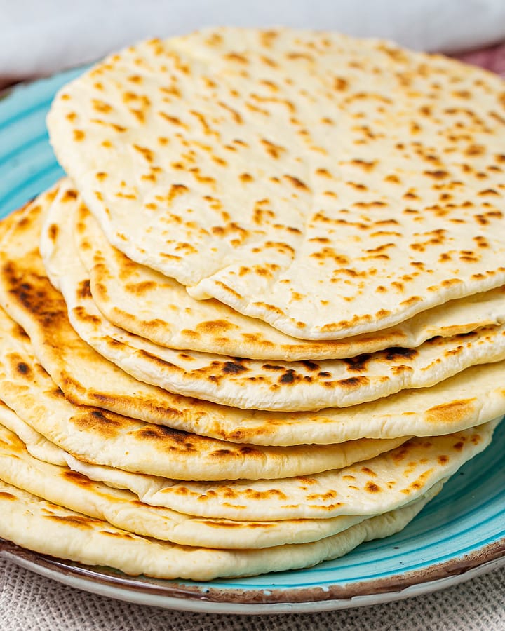 Stack of cooked flatbreads on a teal plate with charred spots visible, suggesting they are freshly grilled.
