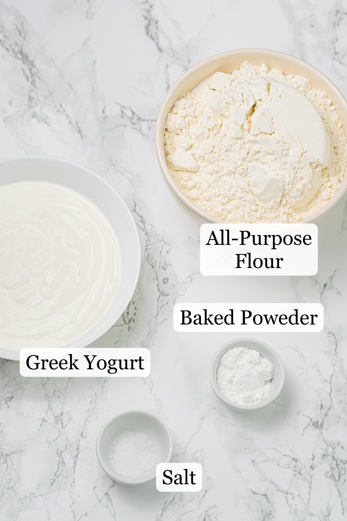 Ingredients for flatbread recipe including bowls of flour, yogurt, baking powder, and salt on a marble countertop.