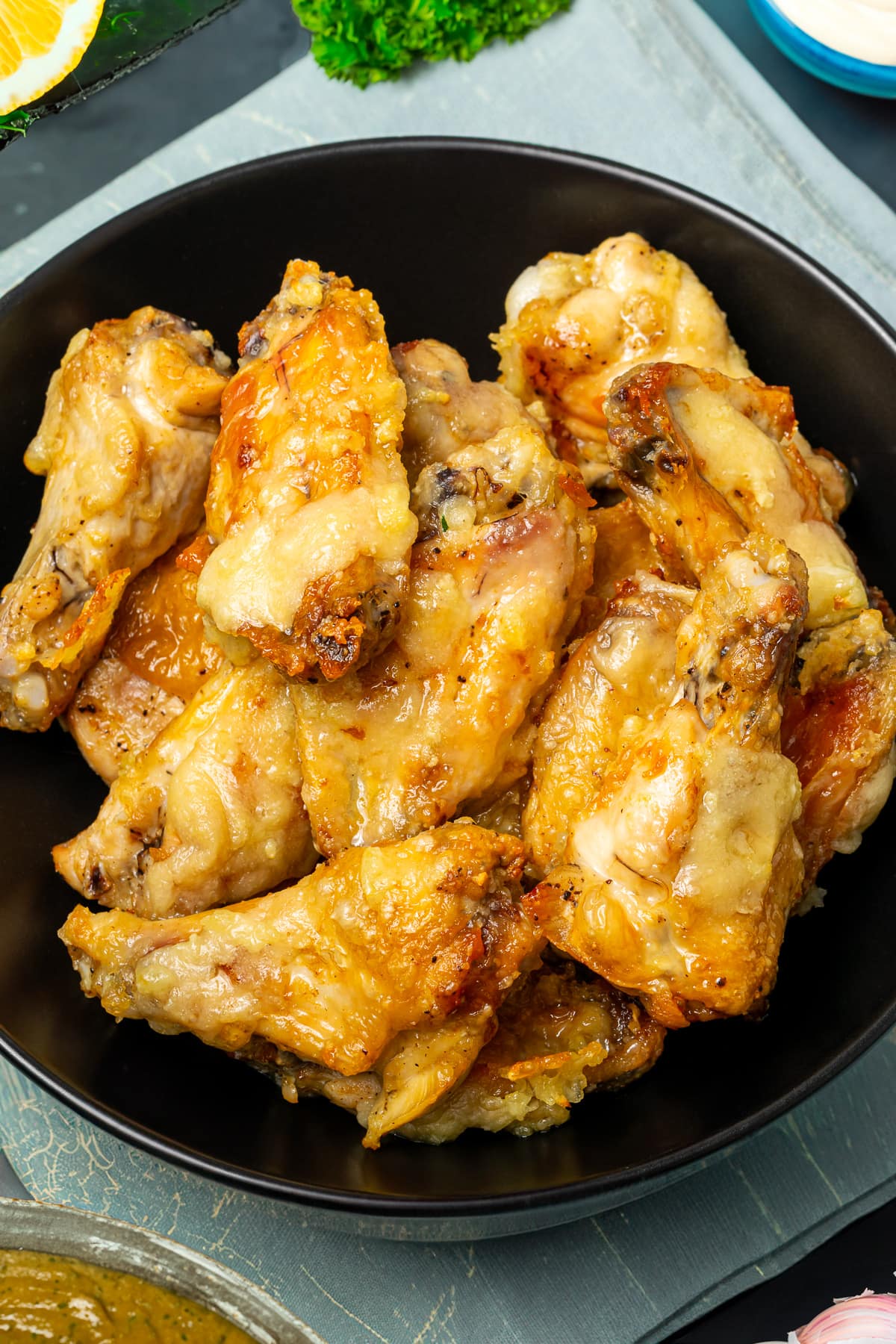 A bowl of golden garlic chicken wings ready to be served, with parsley and lemon in the background.
