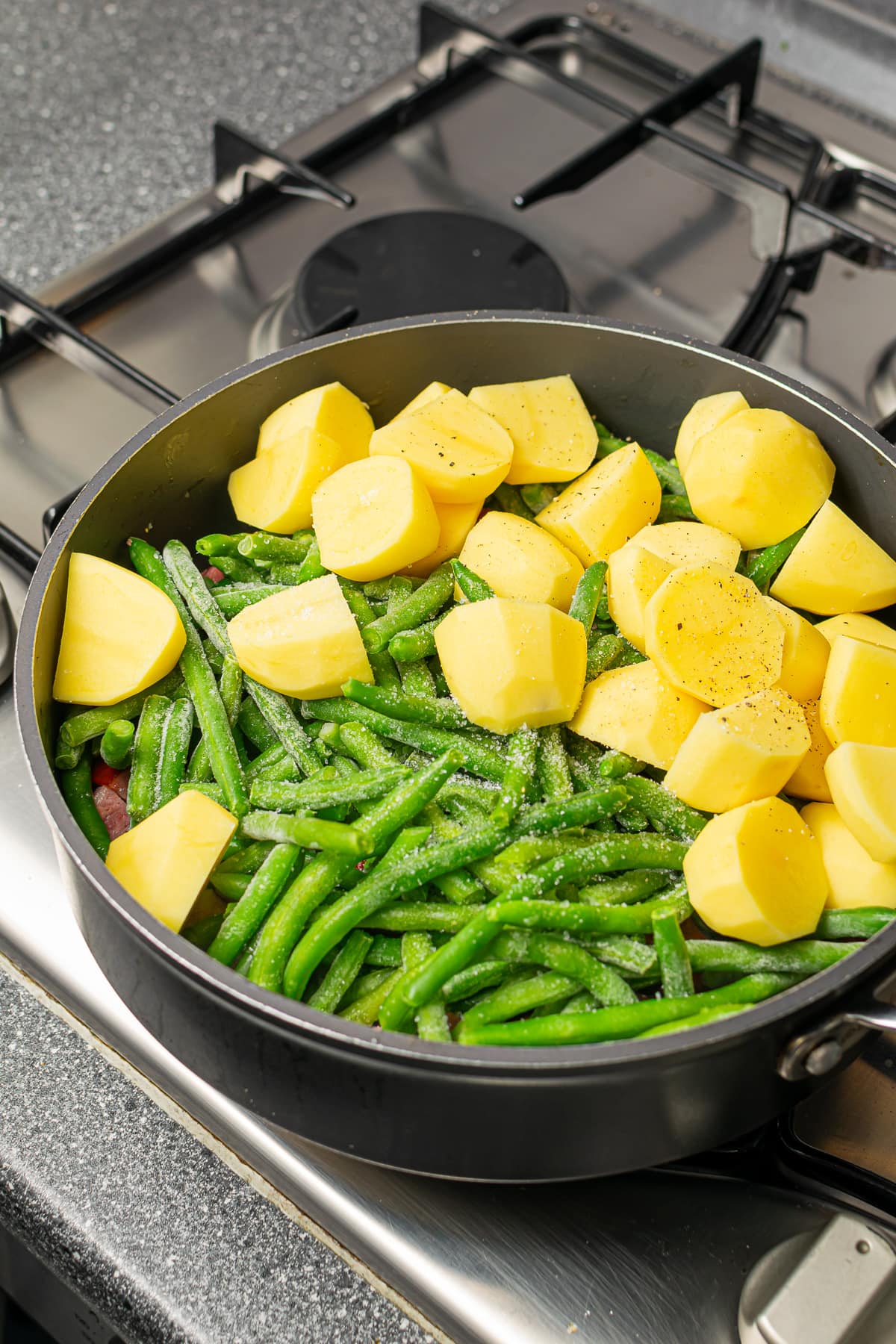 A skillet with sliced potatoes and green beans added to the sautéed kielbasa and onions.