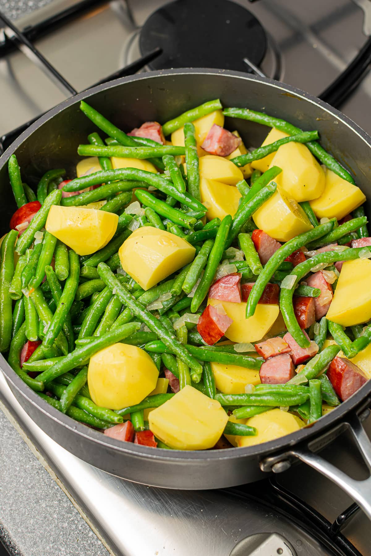 The skillet showing the potatoes, green beans, and kielbasa mid-cooking process.