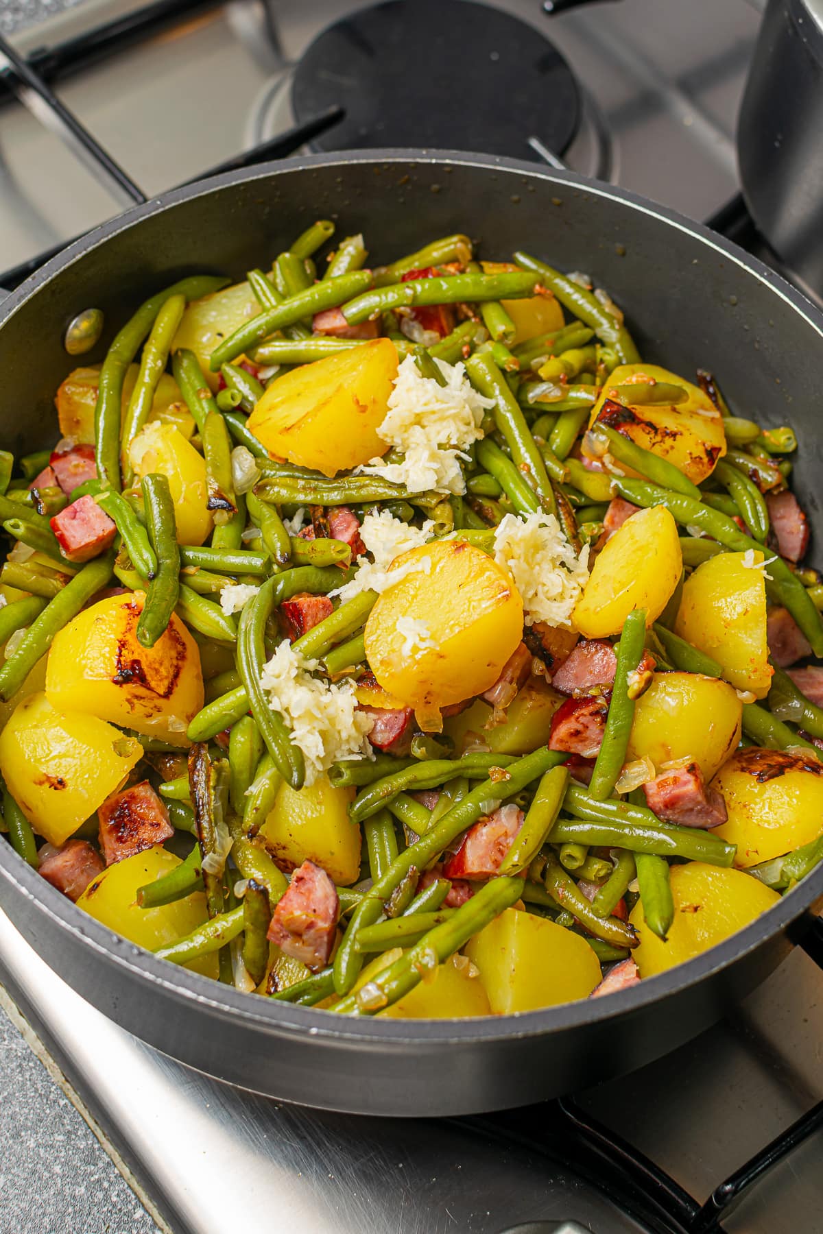 The cooked dish of green beans, potatoes, and kielbasa in a skillet, ready to be served.