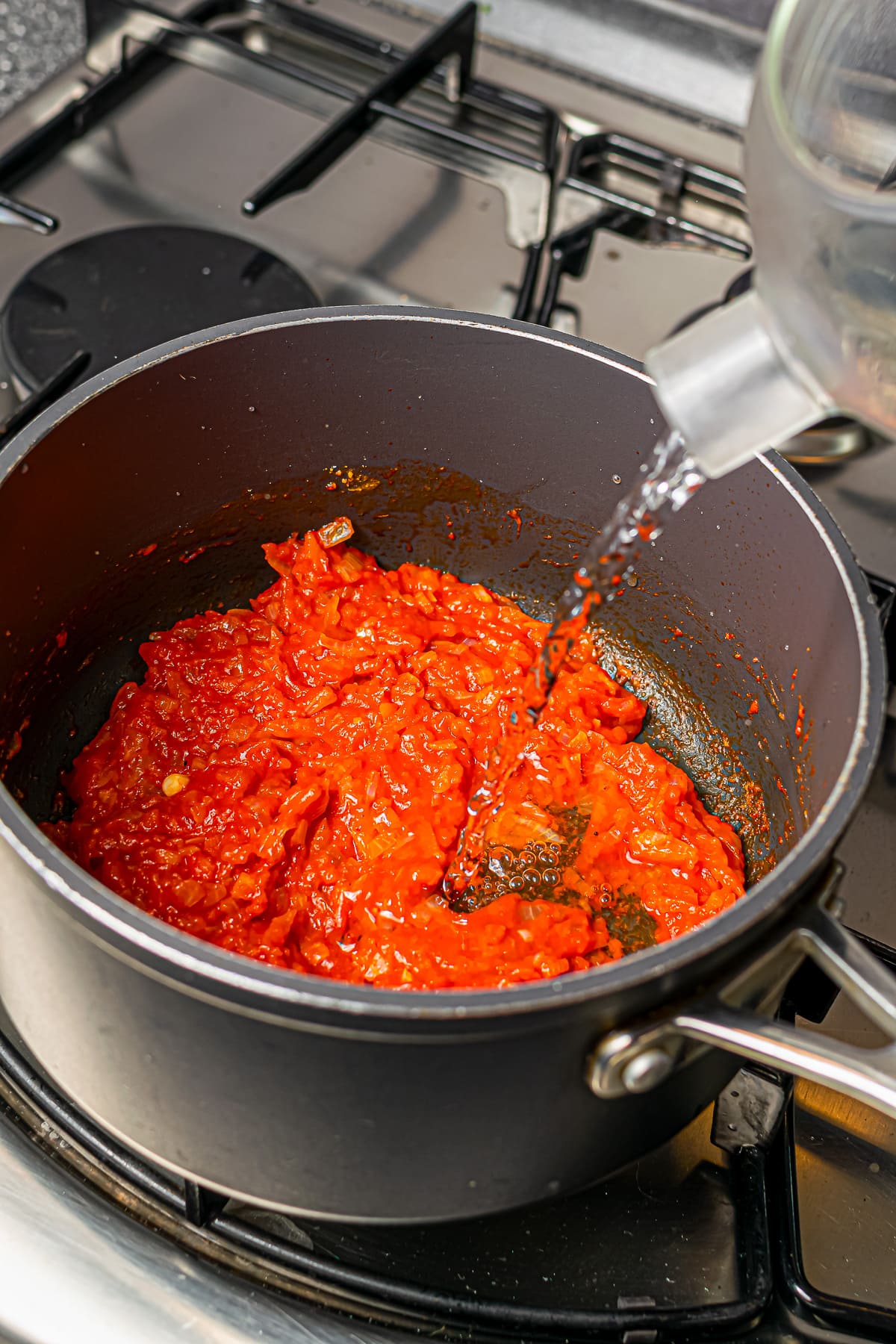 Water being poured into a pot containing a tomato-based soup mixture on the stove.