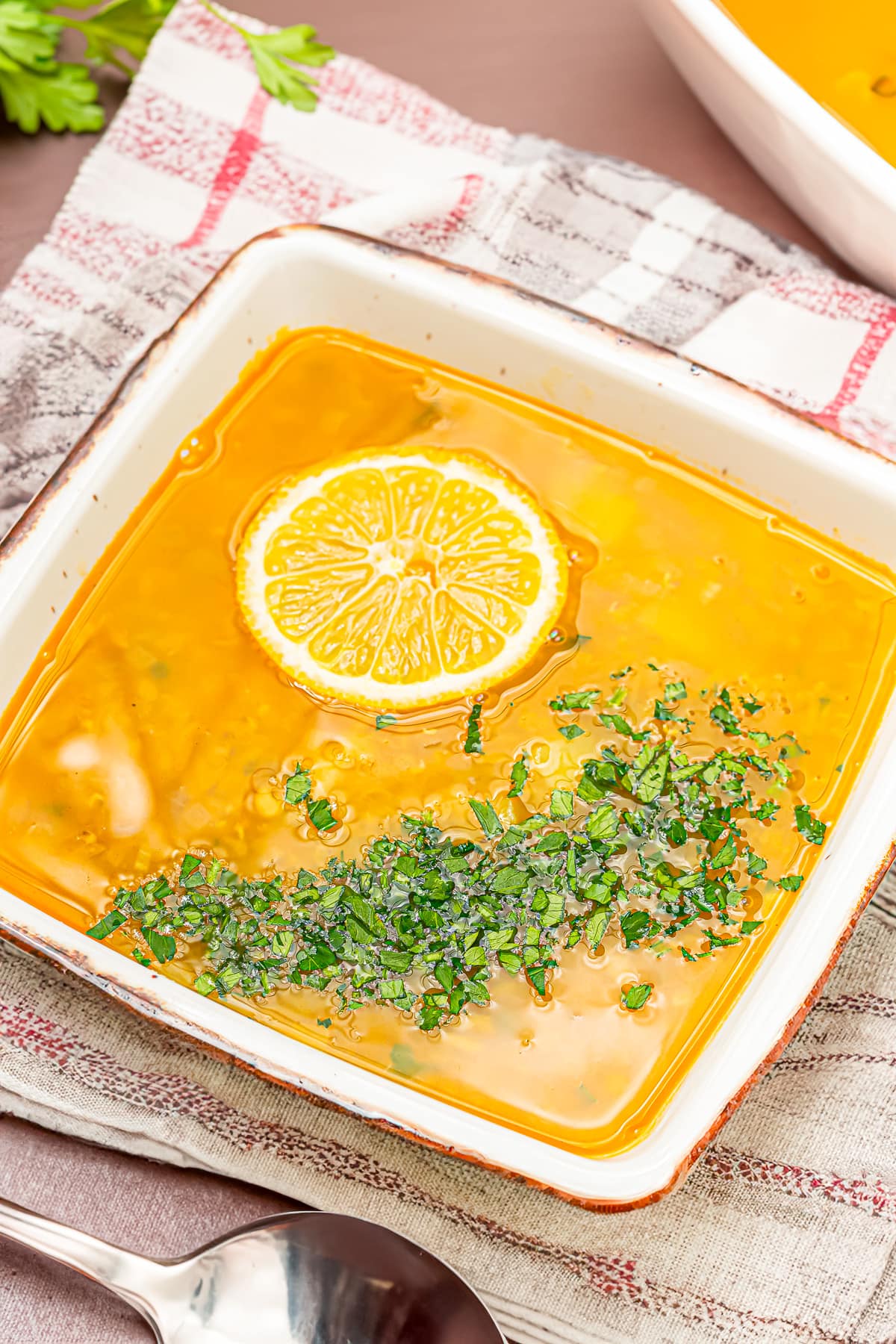 Rectangular dish filled with lentil soup garnished with a lemon slice and chopped herbs.