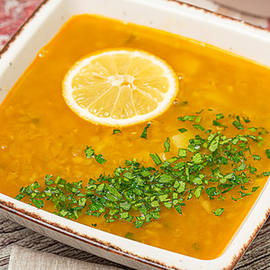Rectangular dish filled with lentil soup garnished with a lemon slice and chopped herbs.