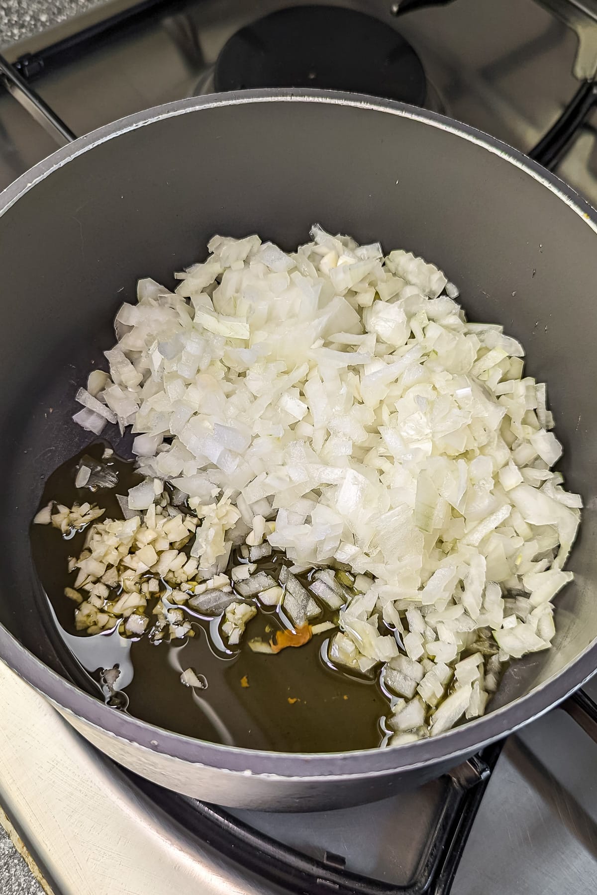 Chopped onions and garlic sautéing in a pot with olive oil.