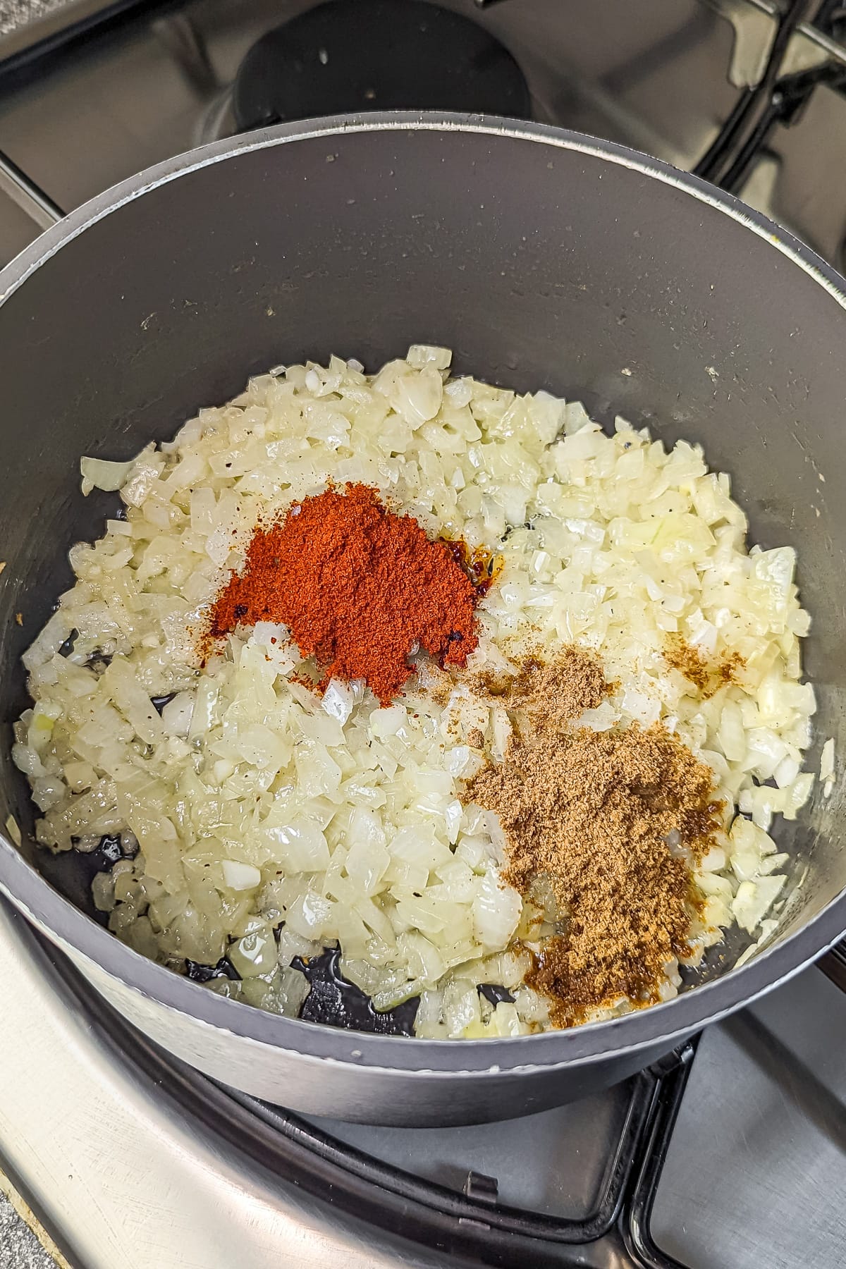 Spices including cumin and paprika added to the sautéed onions in the pot.