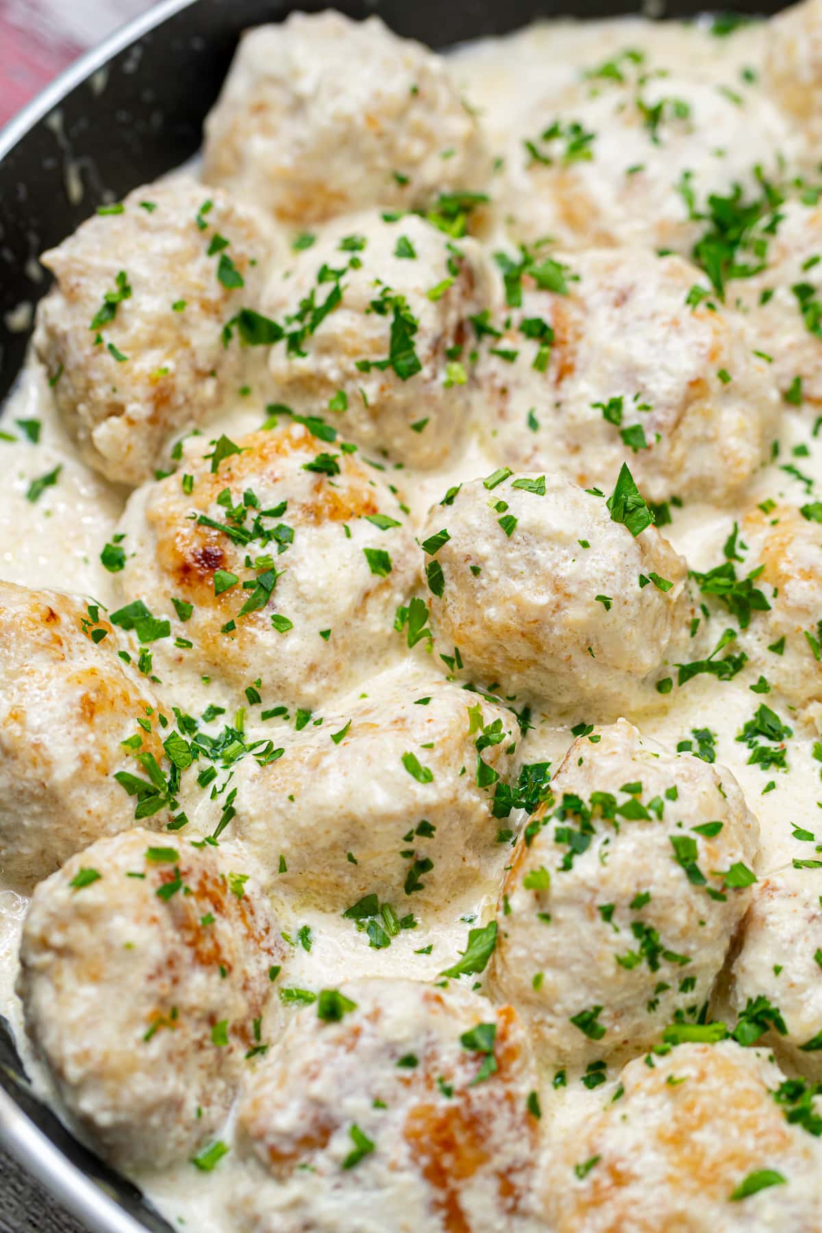 Final dish of meatballs in white sauce garnished with parsley in a pan.