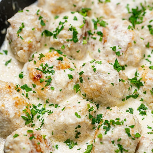 Final dish of meatballs in white sauce garnished with parsley in a pan.