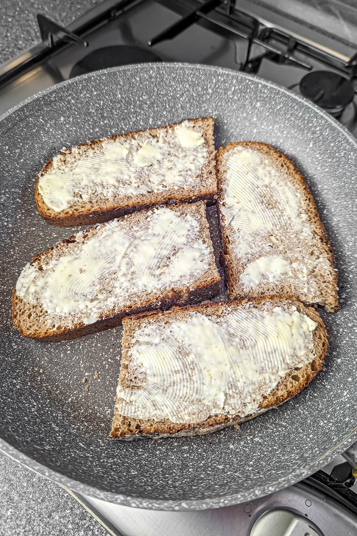 Three slices of brown bread spread with butter in a frying pan.