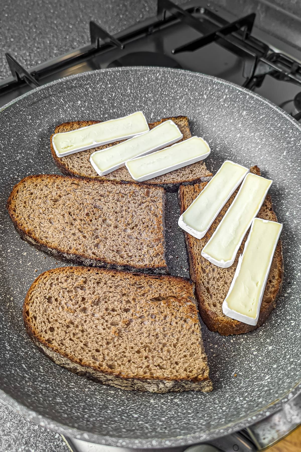 The buttered bread now topped with slices of white cheese in the frying pan.