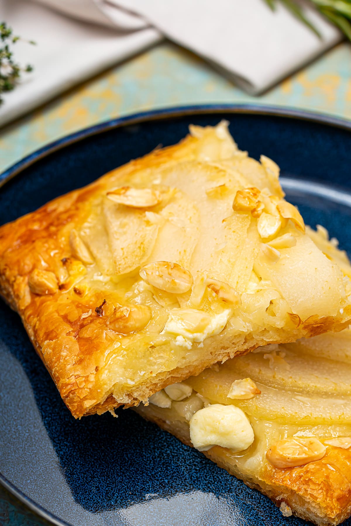 A single slice of pear and feta tart on a blue plate, showcasing the flaky pastry layers and toppings.