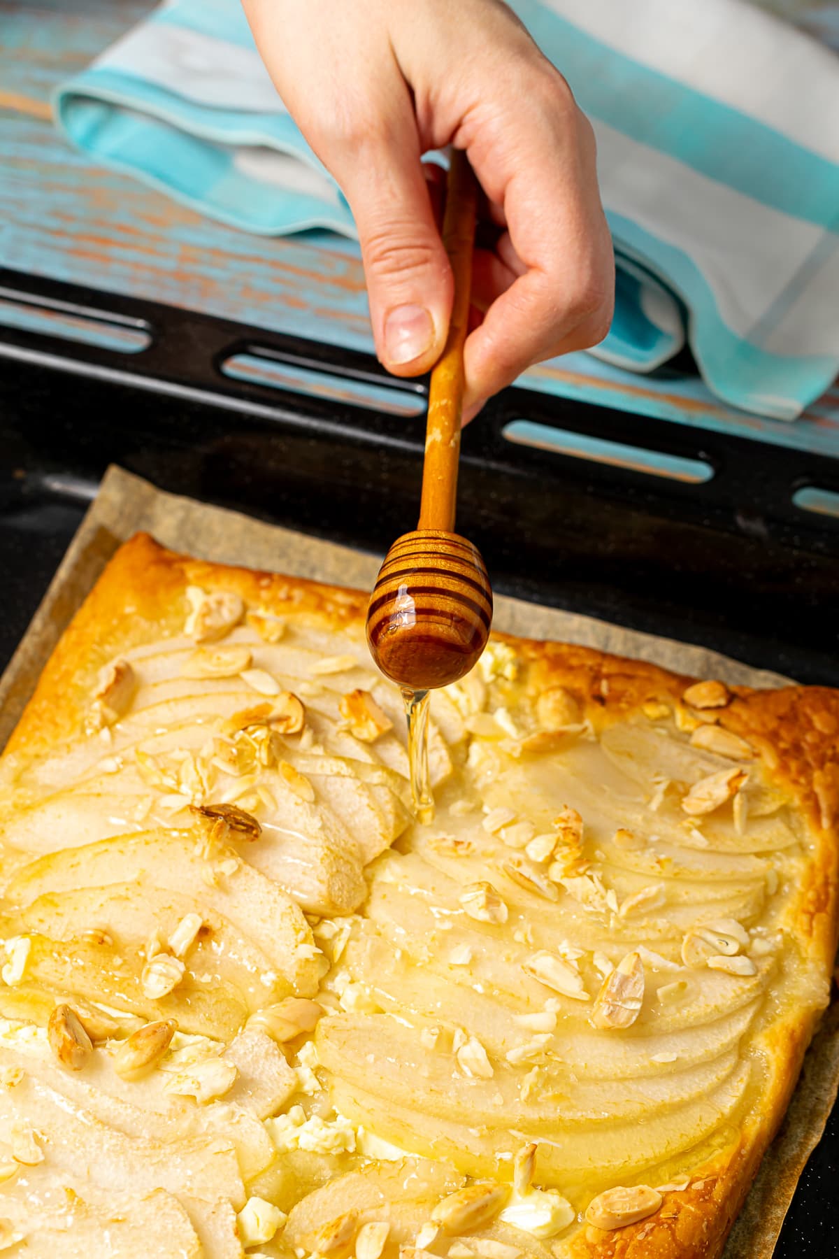 Drizzling honey over a freshly baked pear and feta tart with almond toppings.