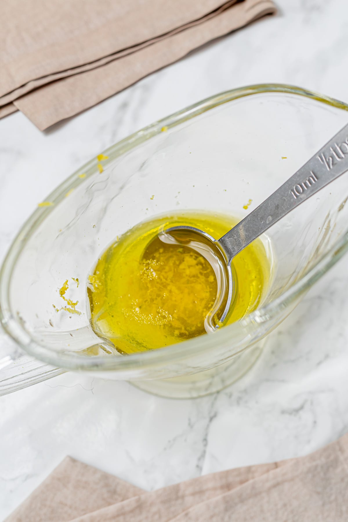 Lemon zest and olive oil dressing in a glass measuring cup.