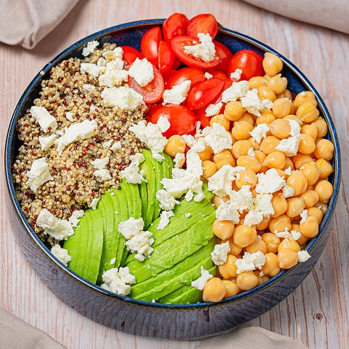 Quinoa, chickpeas, avocado, and cherry tomatoes in a blue bowl before dressing.