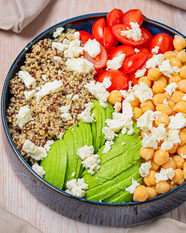 Quinoa, chickpeas, avocado, and cherry tomatoes in a blue bowl before dressing.