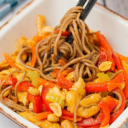 A close-up of teriyaki chicken soba being lifted with chopsticks, showcasing the noodles and vegetables.
