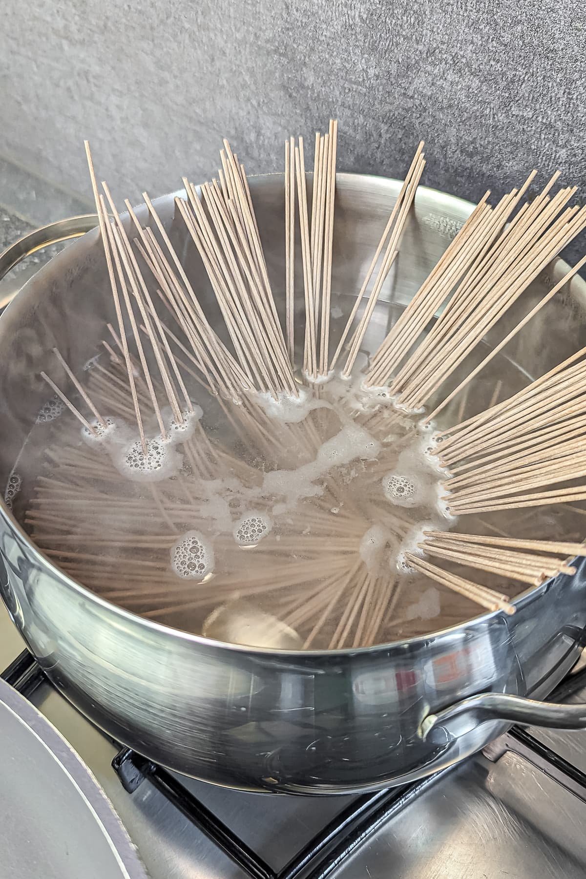 Soba noodles boiling in a pot of water on a stove.