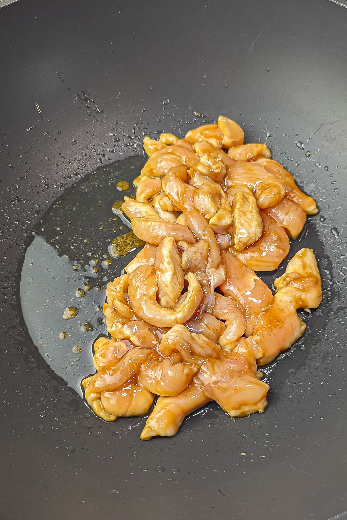 Sliced chicken breast cooking in a non-stick pan coated in teriyaki sauce..