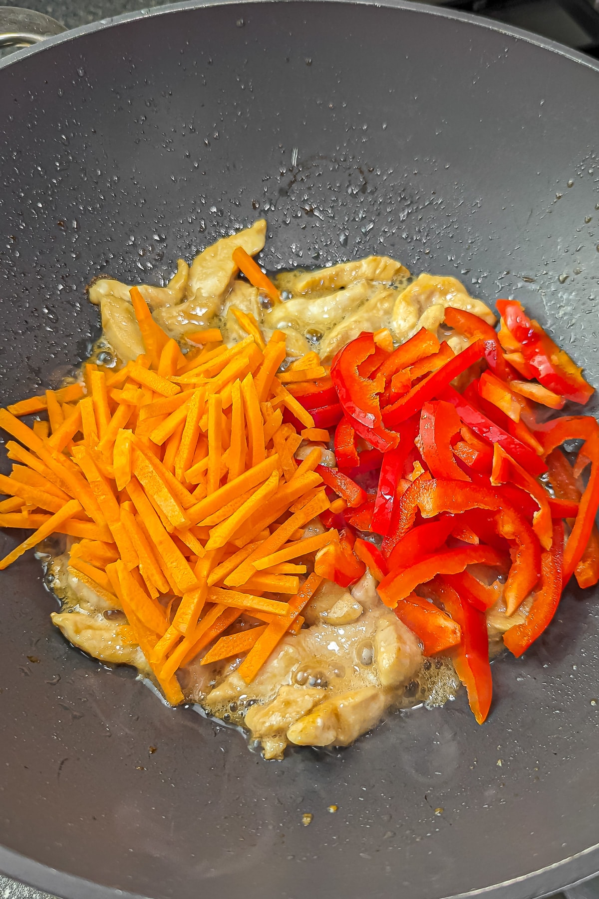 Cooked chicken in a pan with added sliced carrots and red bell pepper.